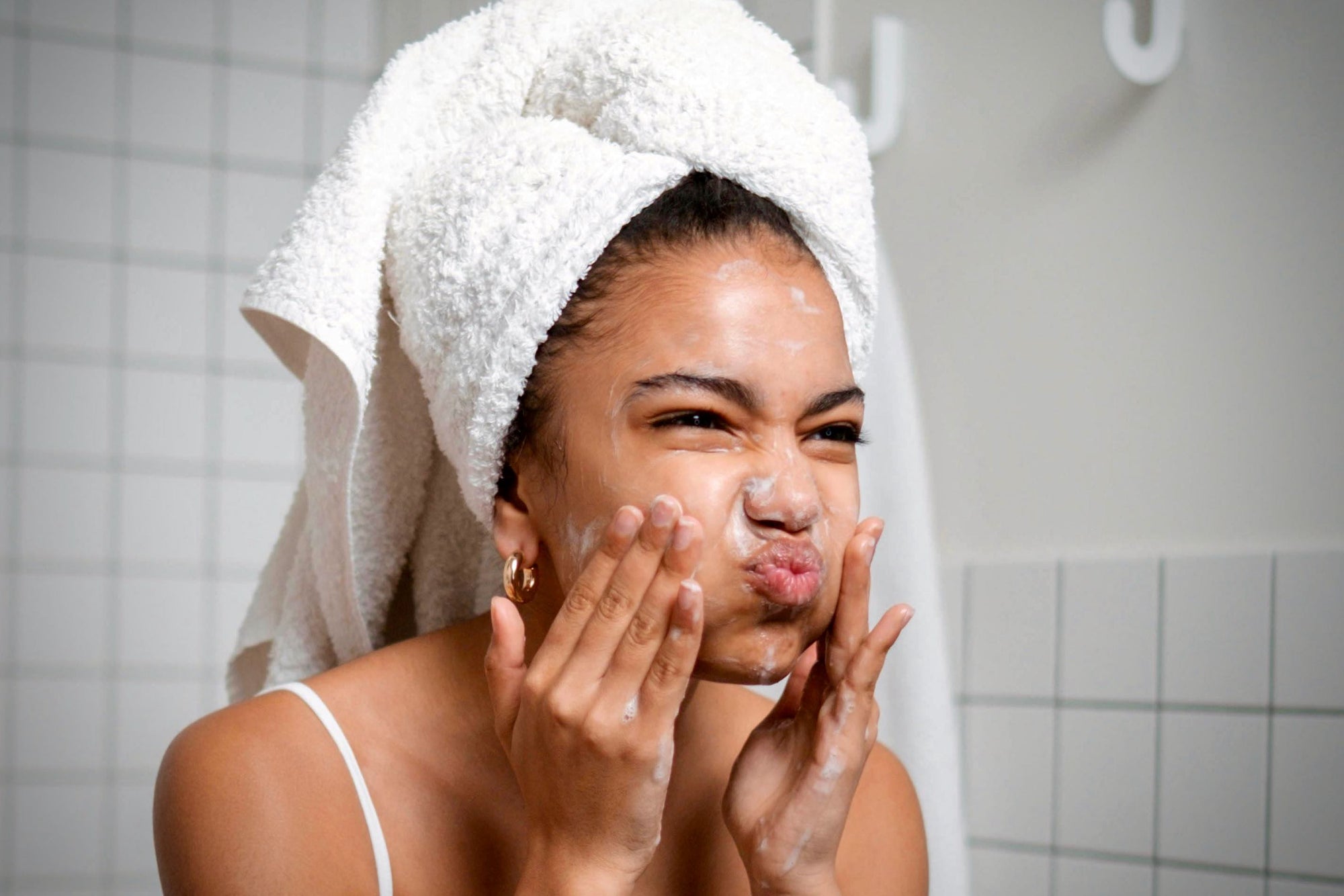 Young woman applying face cream, looking dissatisfied